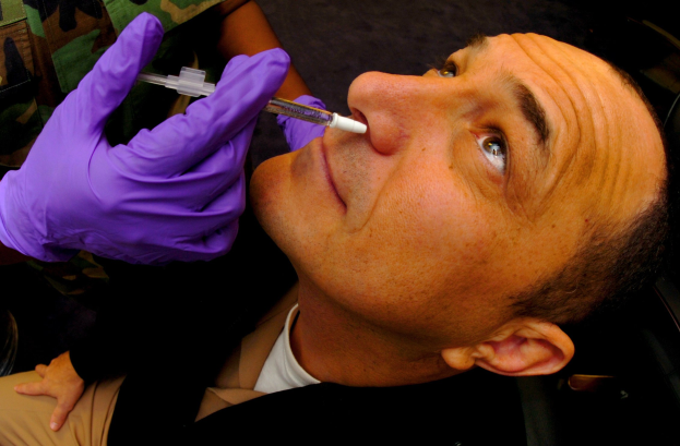 Ein Arzt in lila Handschuhen verabreicht einem Mann ein Vakzin mit einer Spritze im Mund.