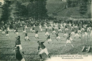Black and white photo of people playing soccer on a grassy field with trees, buildings, and a clear sky in the background, dated "Fête de Gymnastique du 19 août 1923".