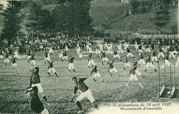 Black and white photo of people playing soccer on a grassy field with trees, buildings, and a clear sky in the background, dated "Fête de Gymnastique du 19 août 1923".