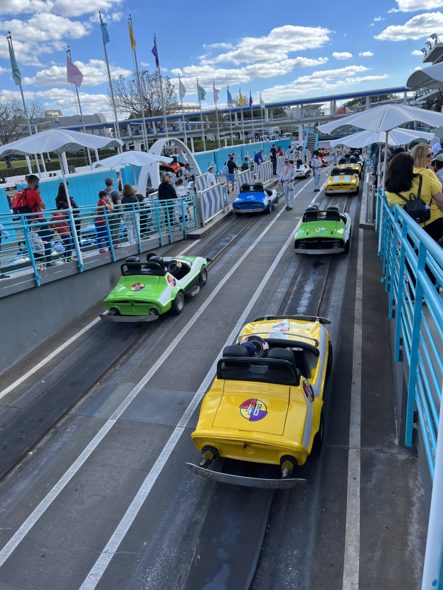 Eine Gruppe von Menschen, die auf einer Achterbahn in Disney's Hollywood Studios fahren, umgeben von Geländern und Fahnen, mit Bäumen und Gebäuden im Hintergrund unter einem bewölkten Himmel.