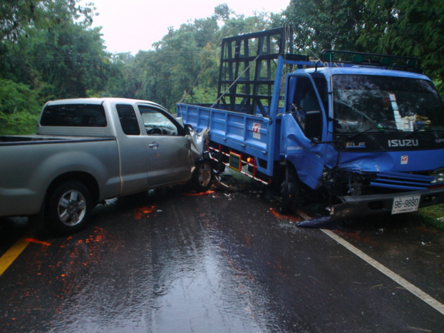 Ein schwerbeschädigtter Lastwagen mit eingedrückter Front und eingebeulter Karosserie liegt am Rande einer Straße, umgeben von Bäumen unter einem klaren blauen Himmel.