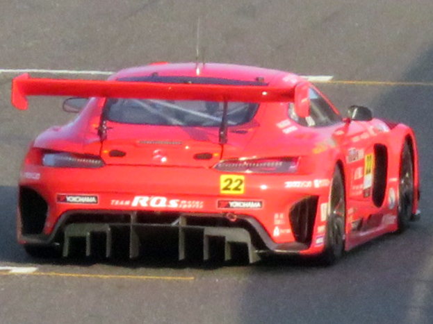 Ein leuchtend roter Porsche 911 GTS Rennauto mit einer großen Heckflosse und Spoiler, das auf einer Rennstrecke fährt.