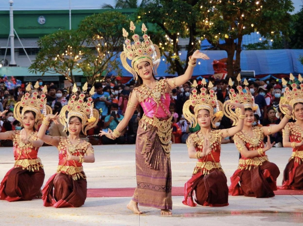 Eine Gruppe von Frauen in traditioneller Thai-Tracht tanzt vor Publikum im Freien.