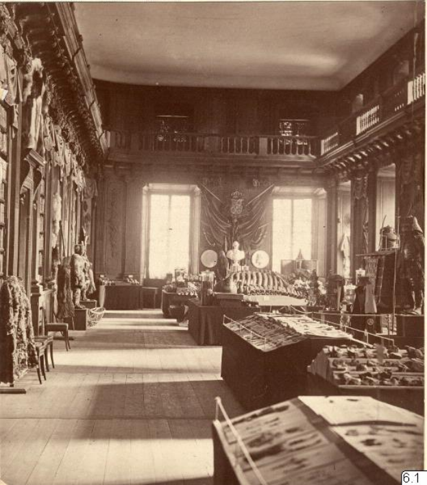 Ein altes Schwarz-Weiß-Foto eines Raums voller Tische, Stühle, Skulpturen an den Wänden, Fenstern, Vorhängen, Geländern und anderen Gegenständen mit der Aufschrift "Museum of Fine Arts, London" unten.