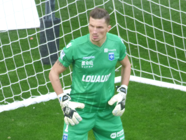 Ein Torwart in grüner Uniform steht auf grünem Rasen vor einem Fußballtor, Handschuhe tragend.
