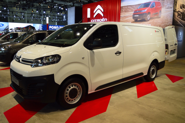 Ein weißer Citroën Berlingo Van auf einer Automesse umgeben von schwarzen Schlafzimmermöbeln, mit Wänden geschmückt mit Brettern und Lichtern.