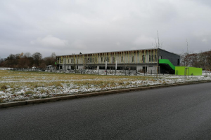 Ein großes Gebäude an der Seite einer Straße, umgeben von Gras und Schnee, mit verstreuten Werkzeugen und Materialien, die auf Renovierung hinweisen, vor dem Hintergrund von Bäumen und einem klaren blauen Himmel.