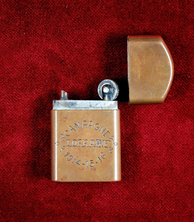 Ein Messingfeuerzeug mit eingravierter Inschrift liegt auf einem roten Tuch.