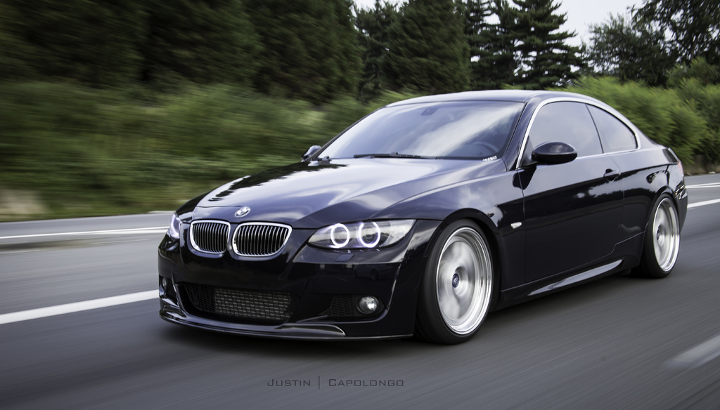 Ein schwarzer BMW auf einer Straße mit Bäumen im Hintergrund.