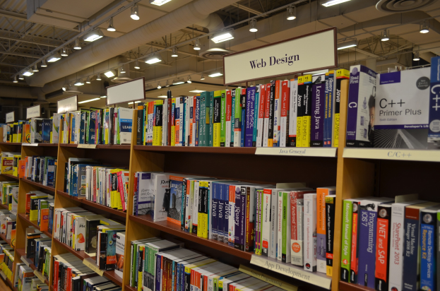 Ein Bibliotheksinneres mit Bücherregalen, die mit Büchern, Texttafeln, Deckenlampen und sichtbaren Rohren gefüllt sind.