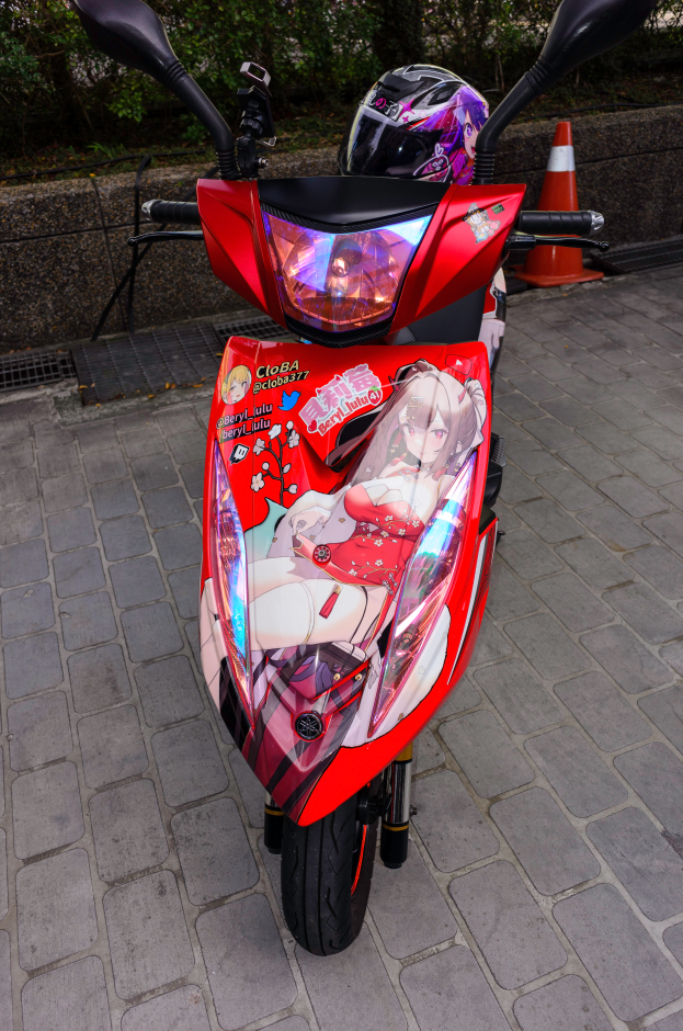 Ein oranger E-Scooter steht am Straßenrand mit einem Helm daneben, mit einer Verkehrskegel, einer Wand und Bäumen im Hintergrund.
