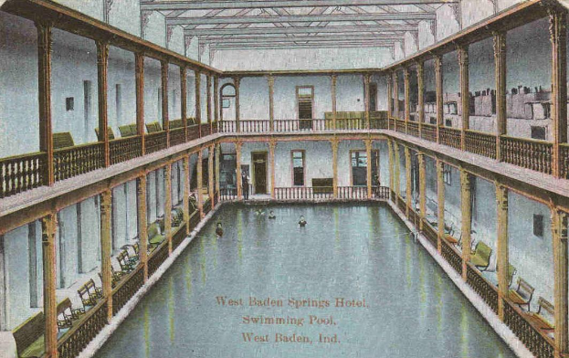 Eine alte Postkarte zeigt ein Hallenbad im West Baden Springs Hotel mit schwimmenden Menschen und verschiedenen architektonischen Elementen drumherum.